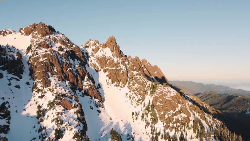 An ascending and looking down drone shot of a snowy peak in the Olympic mountains taken from just outside the national park at sunset