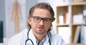Close up portrait of handsome middle-aged Caucasian male doctor therapist looking at camera and speaking while sitting in cabinet, video conference consultation, medic concept, healthcare, medicine