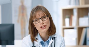 Close up portrait of young beautiful serious female Caucasian doctor in glasses sitting in hospital and speaking looking at camera explaining treatment, telling analysis results, healthcare worker