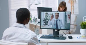 Over shoulder view of male doctor having online video conversation consulting with African American specialist co-worker on computer in clinic, internet consultation about treatment and vaccination
