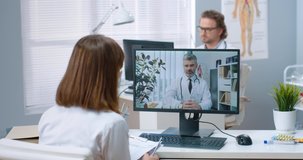 Over shoulder view of woman specialist talking on online video call with Caucasian middle-aged male doctor on computer sitting in cabinet, experienced physician consulting nurse on internet conference