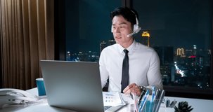 Time-lapse photography of Asian overtime businessman wearing headset uses laptop computer to join video meeting with headset in office at night