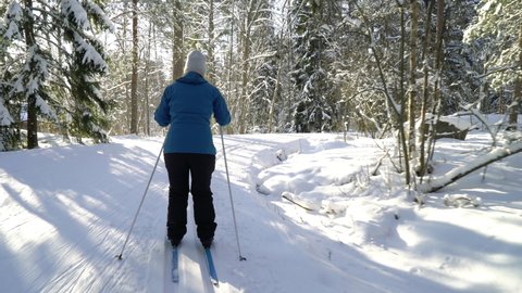 A woman going cross-country skiing in a frozen forest in Finland on a frosty sunny day. Steadicam Tracking Shot.