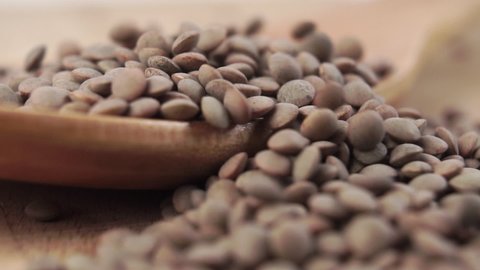 Falling uncooked dry lentils into a wooden spoon on a wood surface in slow motion. Macro shot