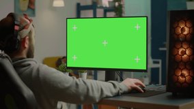 Gamer playing video games on powerful computer with green screen chroma key desktop mock-up display in gaming home studio. Player using RGB keyboard with isolated monitor streaming game wearing