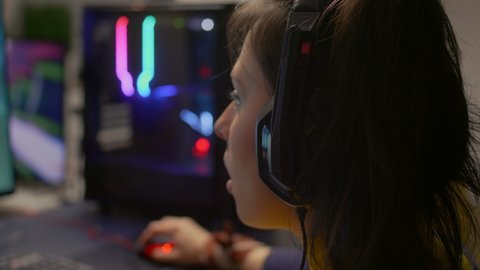 Close-up of pro gamer talking with friends on networks for space shooter virtual competition. Competitive woman with headphones streaming online cyber performing during gaming tournament