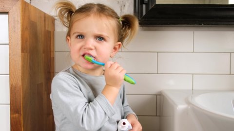 Little girl f brushing her teeth with a toothbrush in bathroom in the morning
