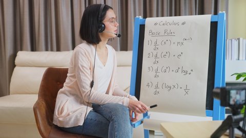 Asian school young woman teacher working from home teach online math subject to student studying from home. Girl points on whiteboard, talk on headphone. Remote education class during covid19 pandemic