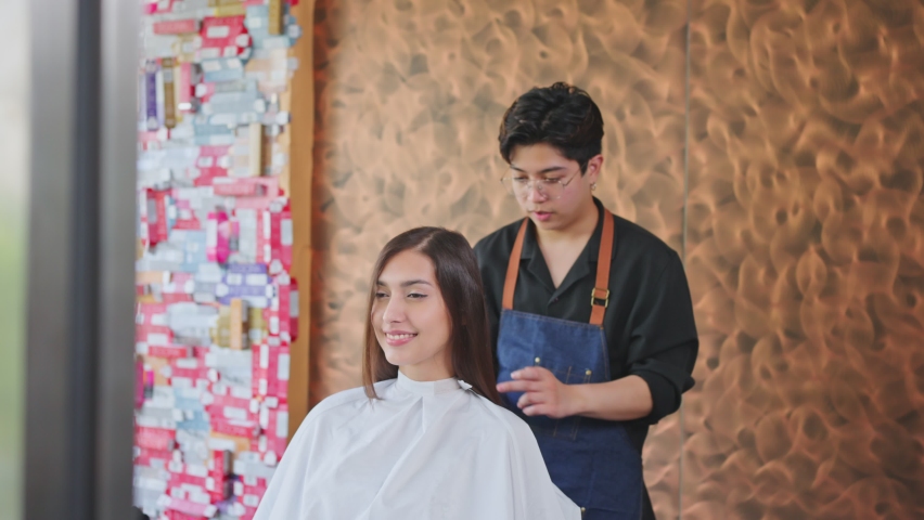 Asian professional male hairstylist setting young beautiful girl customer's hairstyle after cut woman's hair in beauty salon. Hairdresser's pround of his service making arm crossed, looking at camera. Royalty-Free Stock Footage #1068826313
