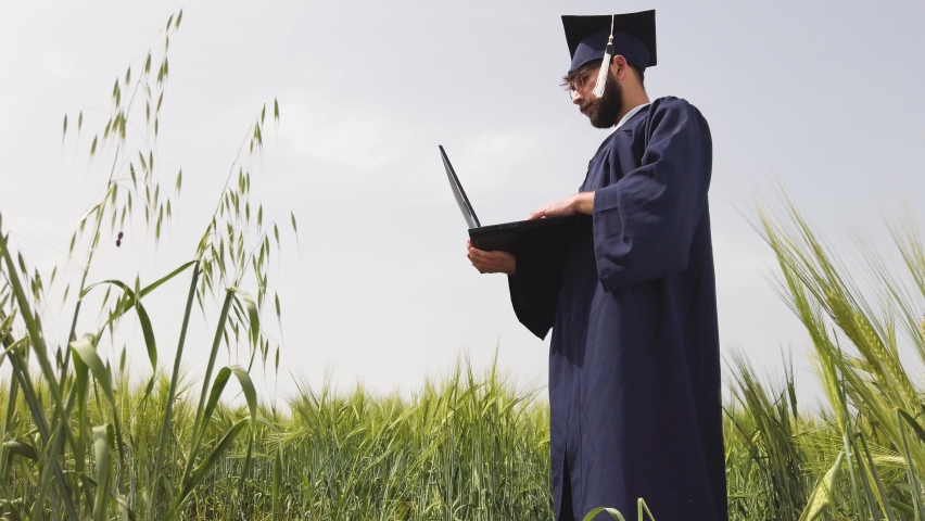 Graduation man alone in nature, looking at laptop, throwing the blue cap. Virtual graduation and social distancing concept