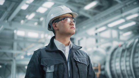 Portrait of a Professional Asian Heavy Industry Engineer Worker Wearing Safety Uniform, Glasses and Hard Hat. Confident Chinese Industrial Specialist Standing in a Factory Facility.