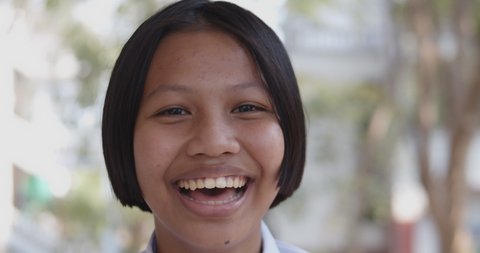 Slow motion scene of a young native Asian female student girl who had pimple on her forehead is smiling happily and shy on the natural bokeh background.