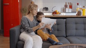 Loving young mother and her little son reading a book on the sofa at home. Slow motion video.