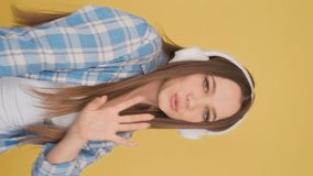 Vertical video Young long-haired woman sings a song and listens to music in large white wireless headphones.