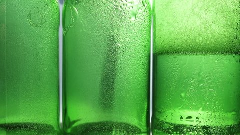 Drops of condensate drains on the green bottles of beer. Water drops  over bottles surface. Spraying water on green glass. Close-up of drops on glass surface. St Patric's day concept. 