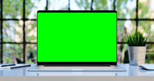 Modern laptop with blank green screen. Static footage with trees swaying or moving in the wind. Home interior or loft office background, 4k 24fps UHD, loop video