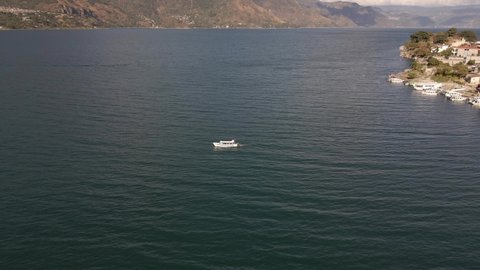 Small Boat cruising from a distance slowly on Lake Atitlan, Guatemala during afternoon Aerial Drone view with mountain landscape
