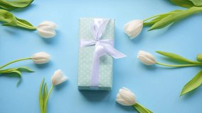 gift, present with white ribbon on blue and flowery with white tulips blue background.Close up.Top view.Zoom in.turquoise polka dot wrapping.