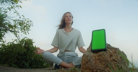 Mock up Meditation Yoga green screen smartphone with Woman sitting in lotus pose on background outdoor