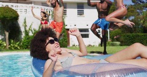 Diverse group of friends having jumping into a swimming pool. Hanging out and relaxing outdoors in summer.