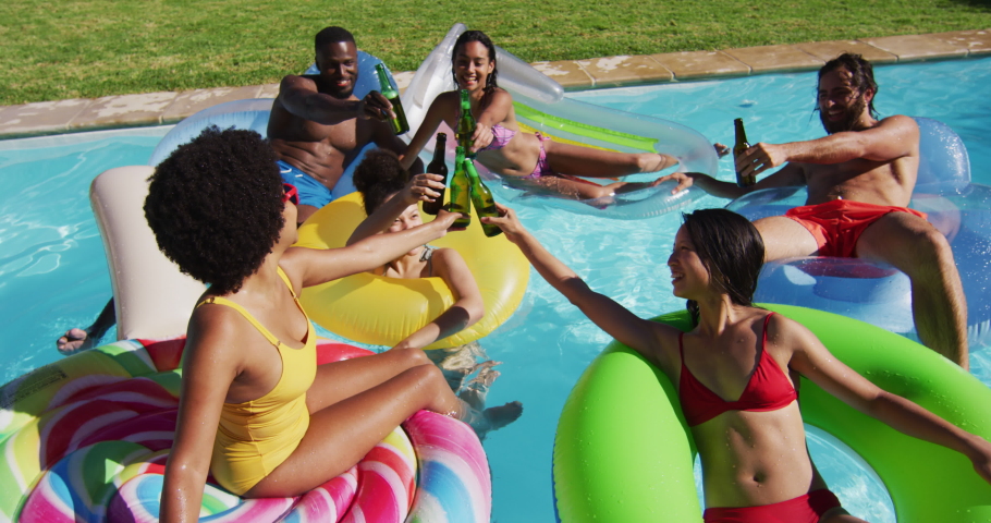 Diverse group of friends having fun playing on inflatables making a toast in swimming pool. hanging out and relaxing outdoors in summer. | Shutterstock HD Video #1068861212