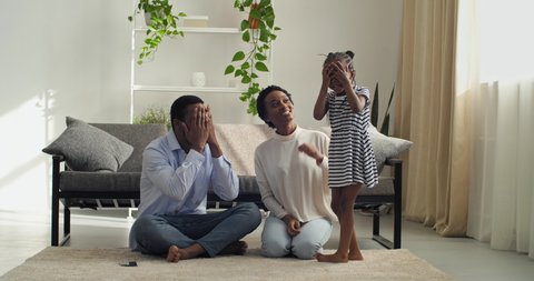 Family playing hide and seek sitting on floor in cozy living room, Afro American parents spend time with their daughter on weekend, covering their eyes with their hands, pretending that they invisible