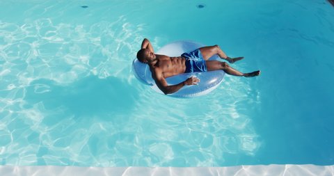Mixed race man having fun sunbathing on inflatable in swimming pool. hanging out and relaxing outdoors in summer.