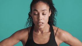 Young attractive African American woman dressed in sport bra hard breathing tired after training over colorful background. Sporty girl
