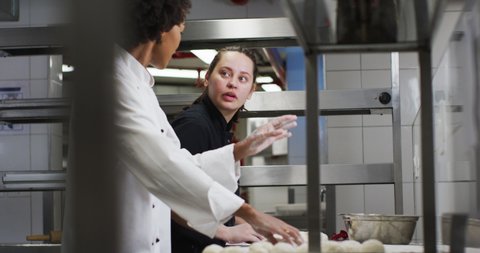 Two diverse female chefs preparing dough and talking in restaurant kitchen. Working in a busy restaurant kitchen.