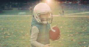 Cheerful happy child in helmet playing American football outdoors in sunny day at public park. Family sports weekend. 4K video.
