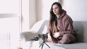 Young and attractive woman is recording video blog with a camera. Happy girl is sitting at home and vlogging.