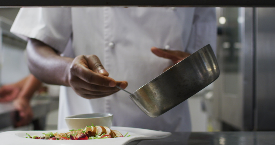 Midsection of african american frmale chef garnishing dish in restaurant kitchen. Working in a busy restaurant kitchen. Royalty-Free Stock Footage #1068866462