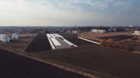 Aerial drone video of plowed spring field covered polyethylene. Agriculture and farming. Fly over field with small greenhouses. 4K drone footage. Top view.