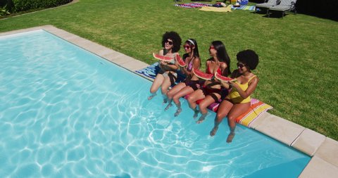 Overhead view of group of diverse girls eating watermelon while sitting by the pool. youth friendship and pool party concept