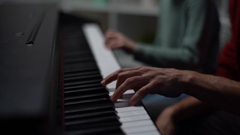 Close-up fingers of child boy playing piano, music teacher sits near and helps with playing during lesson at music school. Kid practicing piano lesson in living room. Shooting in slow motion.