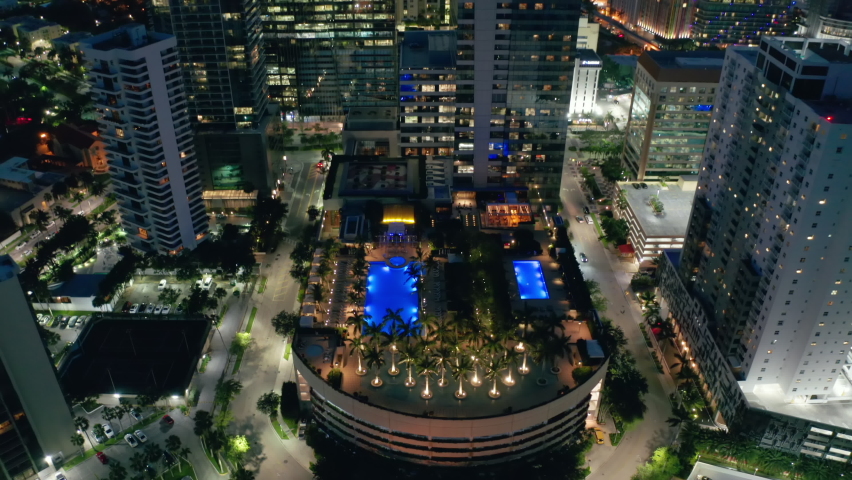 Cinematic top down view on rooftop bar with pool design landscape park with palm trees and multiple fireplaces. Downtown Miami at night, aerial. Modern urban cityscape, drone b roll 4K, travel footage