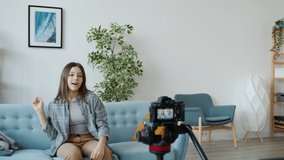 Female teenage blogger is recording video talking to camera then fighting with mother sitting on couch at home. Blogging and family problems concept.