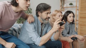 Father and mother mature people are playing video game then doing high-five with children having fun at home. Modern technology and gaming concept.