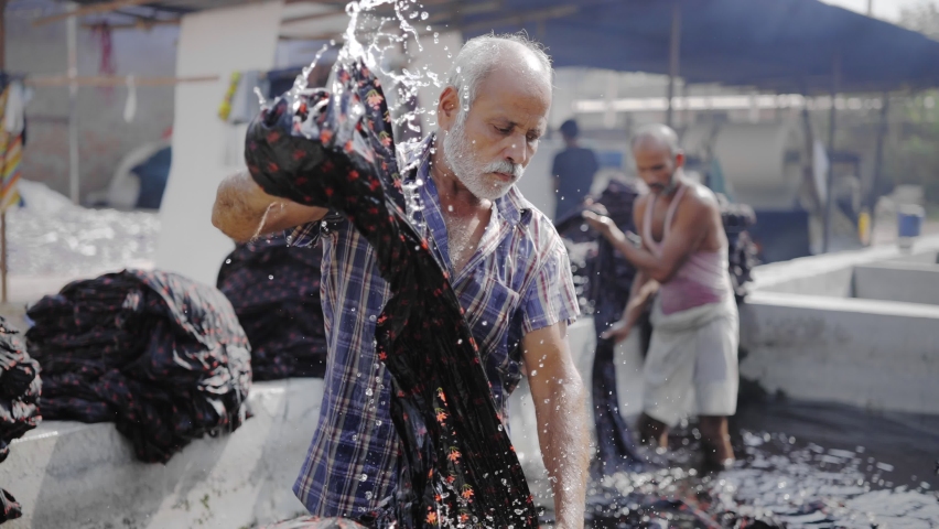 Shot of two Indian laborers removing a long cotton sheet of colored print cloth out of water in the local textile manufacturing company, the concept of restarting or reforming economic activity | Shutterstock HD Video #1068878423