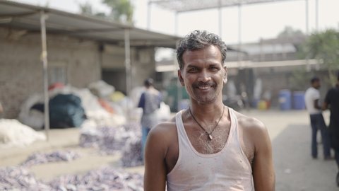 outdoor close-up shot of a happy Indian middle-aged male local factory worker standing outside the plant is smiling, and looking at the camera in a broad daylight
