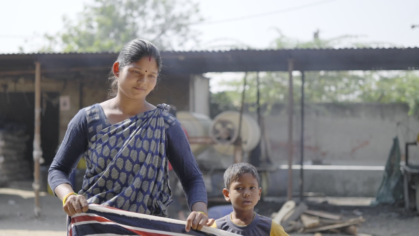 A young married Indian traditional female housewife standing and working in a textile firm with a male child by her side in a broad daylight both looking at the camera. Mothers day concept | Shutterstock HD Video #1068878432