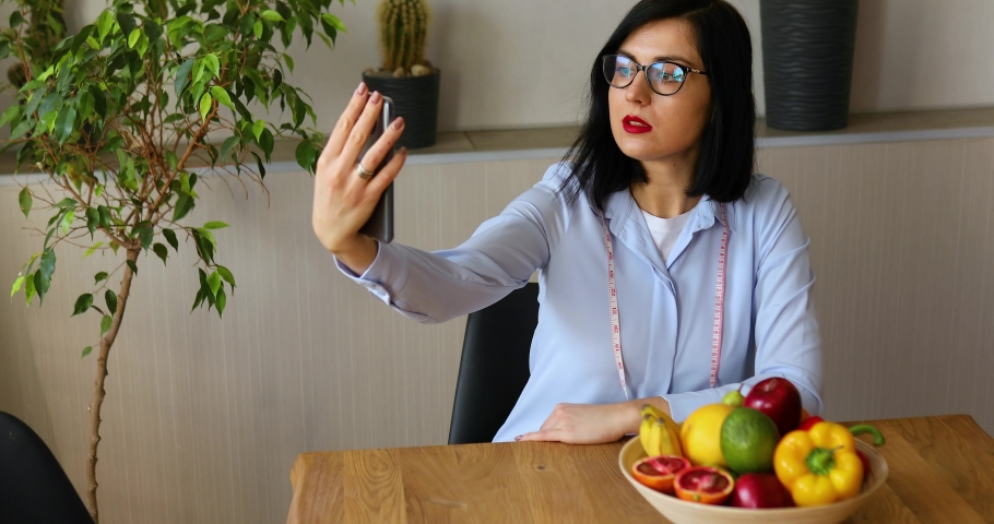 Nutritionist, dietitian woman recording on a smart phone her vlog about healthy eating, healthcare and diet concept. Female nutritionist with fruits working at her des at home. Royalty-Free Stock Footage #1068879497