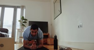 Mixed race male holding plank in living room exercising from home before online work