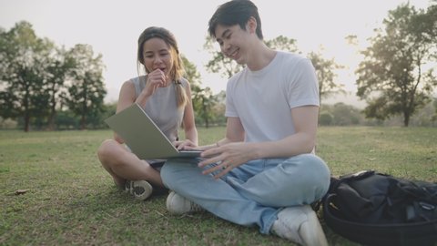 Young adult friends enjoying working together on the outdoor field trip, sit down on the ground green grass inside the park, discussing homework project, friends using laptop brainstorming on project