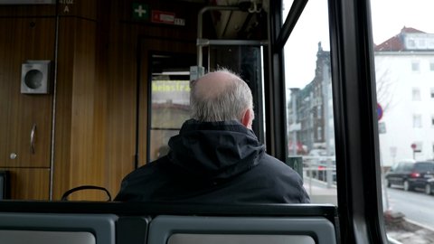 Interior and selective focus, back of old male passenger with hair loss problem wear face protection mask and sit in light rail tram or train in Germany during epidemic of COVID-19 virus.