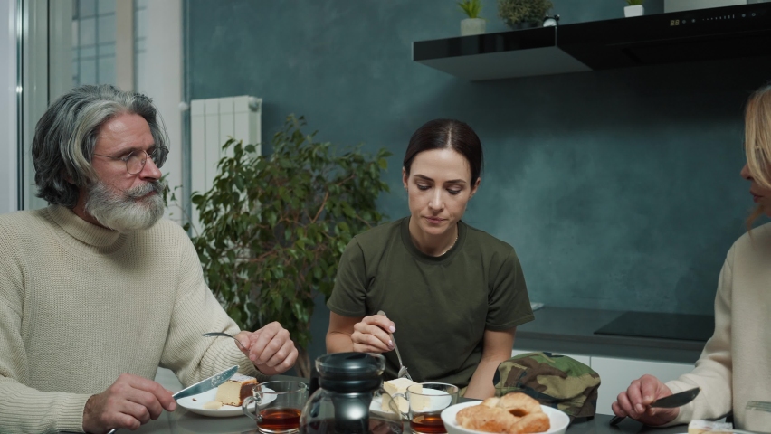 An attractive young woman wearing military uniform is having dinner with her family sitting inside the house