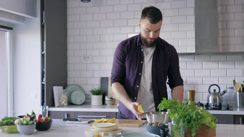 Handsome Young Man Squeezing Lemon on Vegetables Fresh Salad, Salad Dressing, Single Adult Cooking Vegan Healthy at Home in Modern Kitchen on Daylight, Real Time, Handheld