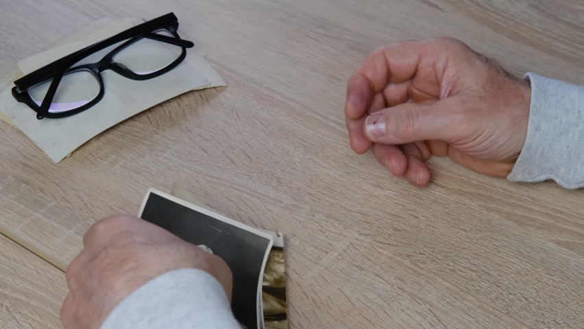 old male hands hold retro family photos over an album with vintage monochrome photographs in sepia color, genealogy concept, ancestral memory, family tree, childhood memories	
