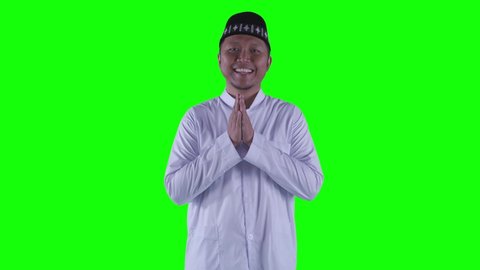 Muslim young man showing congratulate hands gesture Eid Mubarak while smiling at the camera with green screen background. Shot in 4k resolution