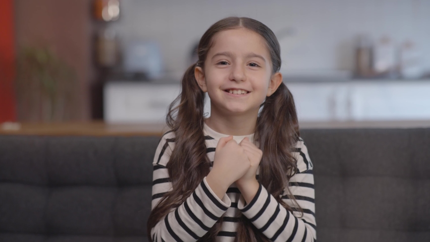 Cute little girl making a heart with her hands and smiling while having a video call. Smiling young beautiful girl showing heart symbol and shape with her hands. Mothers Day. Cam camera view.